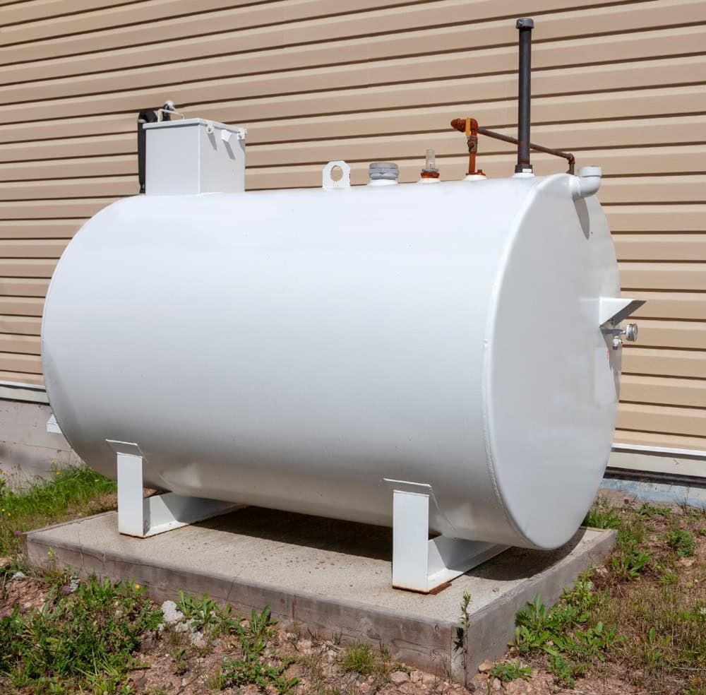 A home heating oil fuel tank standing securely on a concrete slab outdoors, with connected piping visible.