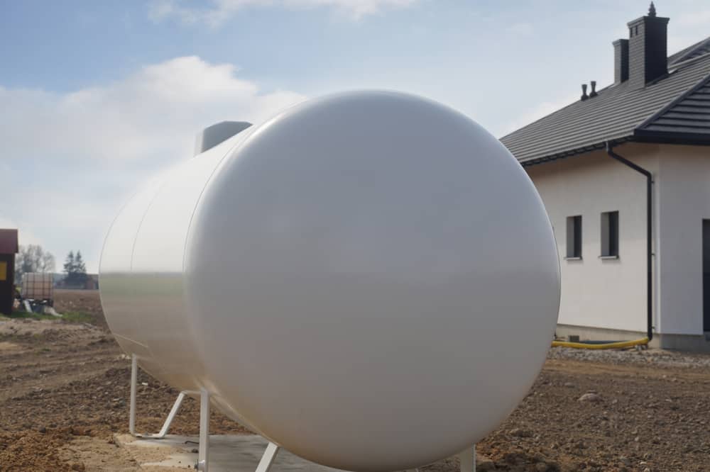 Close-up of a large white horizontal heating oil tank positioned outdoors, with a house visible in the background.