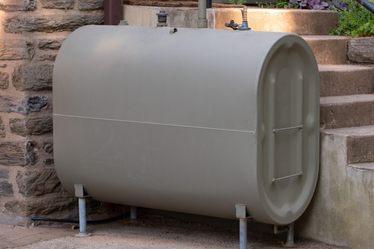 Close-up view of a white horizontal heating oil tank situated outdoors against a brick wall, showing just the rounded end of the tank.