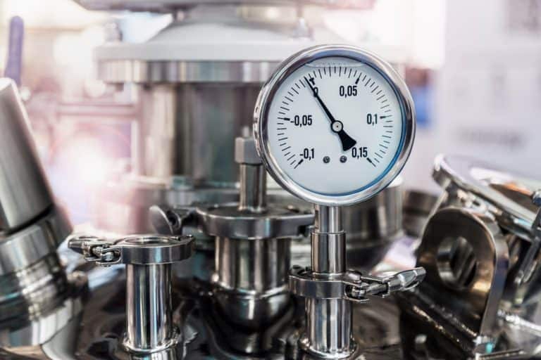 Close-up of a round pressure gauge mounted beside a steel valve, showing measurement markings and a needle indicating system pressure.