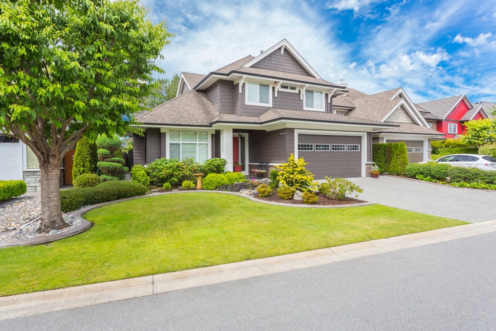 A beautifully manicured garden with neatly trimmed shrubs, colorful flowers, and lush green grass located in front of a luxury home.