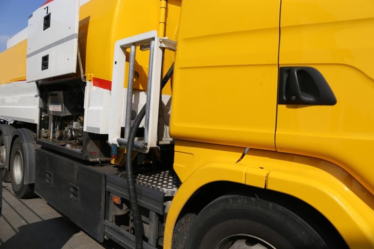 Close-up view of a fuel delivery truck, focusing on the hose and nozzle as oil is being pumped directly into a storage tank during a heating fuel delivery.