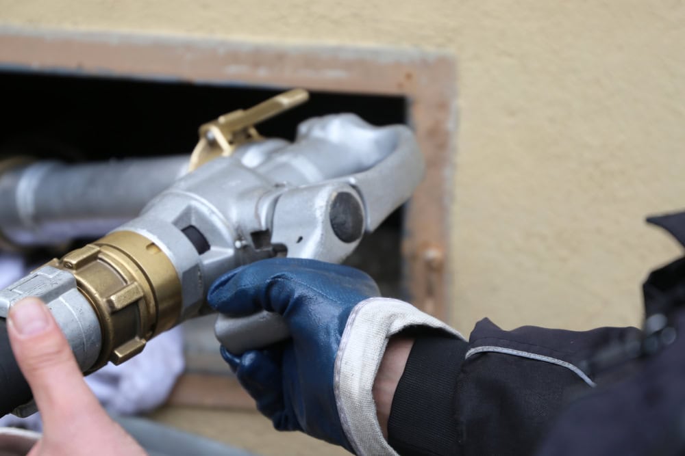 Close-up view of a heating oil delivery truck’s hose and nozzle actively pumping fuel into a storage tank during a home heating oil delivery.