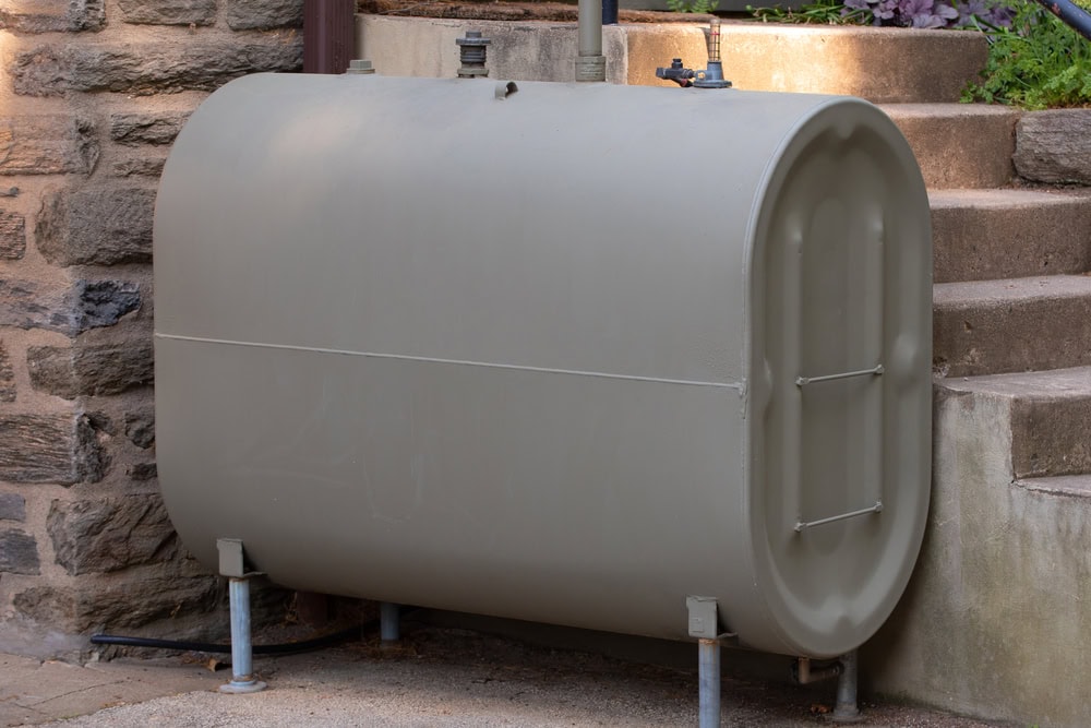 A large steel heating oil tank installed outdoors near a home, designed to store fuel for providing natural energy to power the home’s heating system.