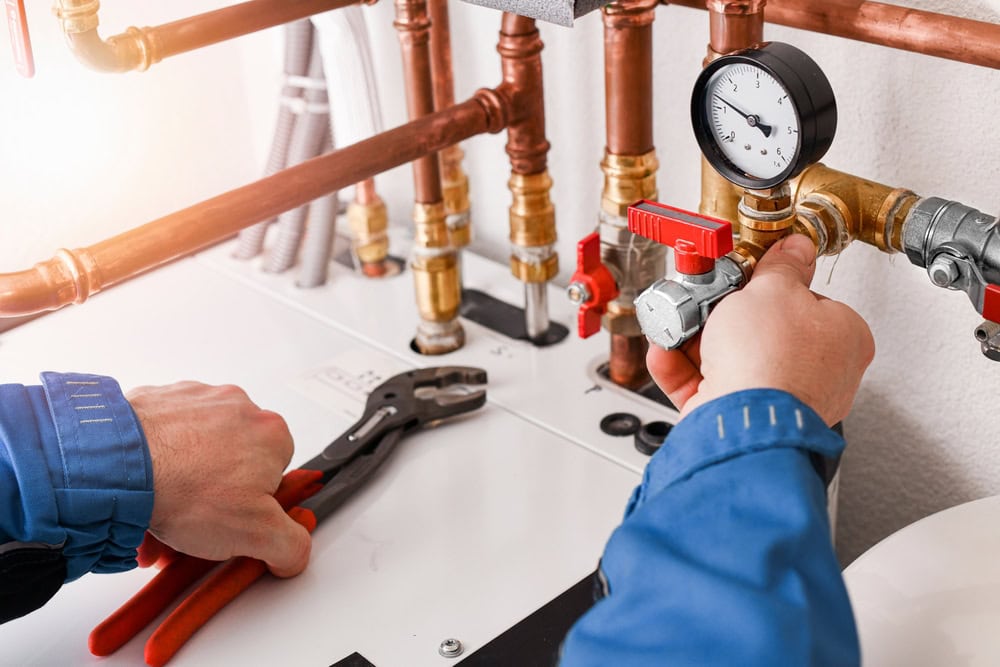 A plumber wearing work overalls and gloves, using specialized tools to install or repair a copper water pipeline, representing a plumbing service or maintenance concept.