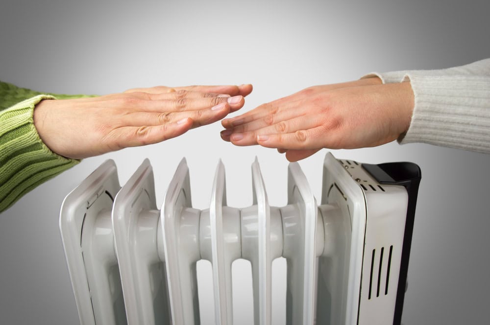 A couple sitting indoors with their hands held out toward an electric heater, warming themselves on a cold day.