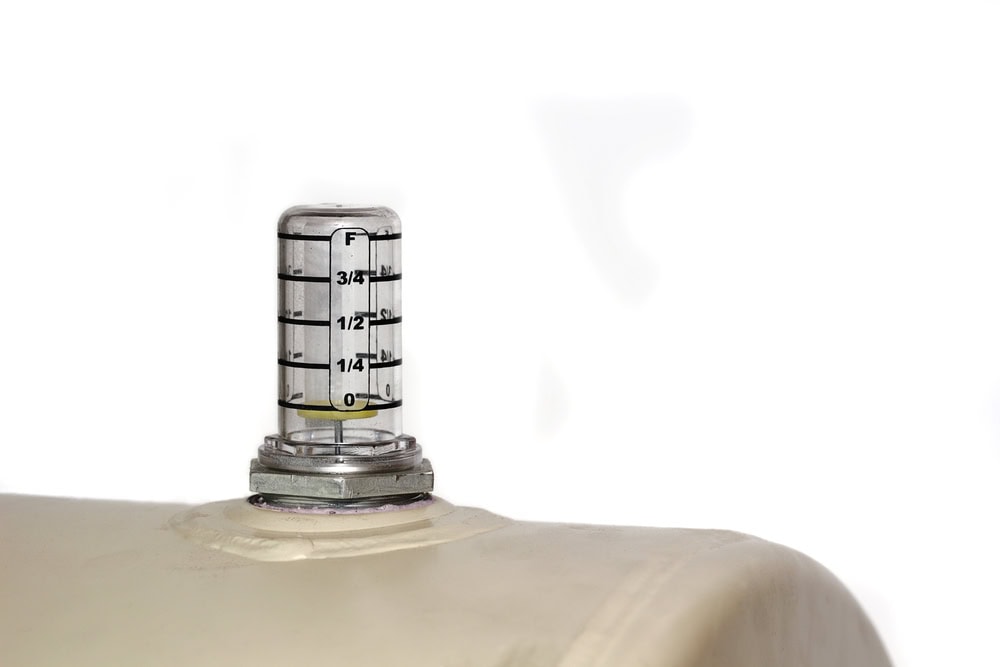 Close-up of a round fuel gauge mounted on a home heating oil tank, with the needle pointing to “Empty,” indicating no remaining fuel.