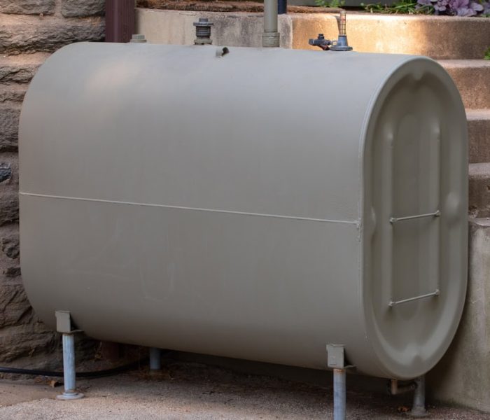 A large steel heating oil tank installed outdoors near a home, designed to store fuel for providing natural energy to power the home’s heating system.