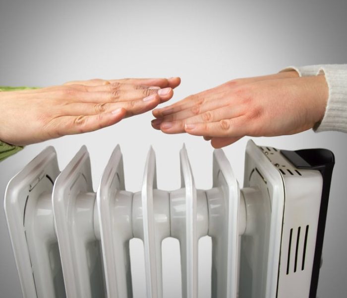 A couple sitting indoors with their hands held out toward an electric heater, warming themselves on a cold day.